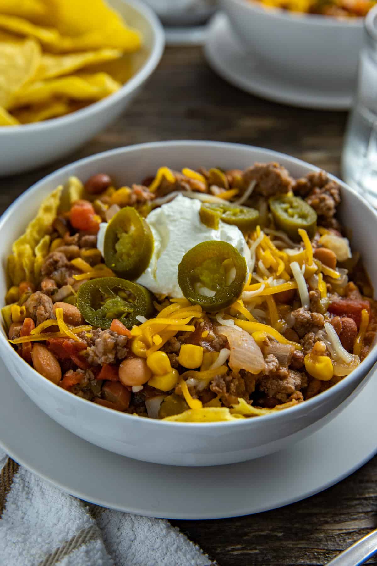 Taco soup in white bowl garnished with corn chips, sour cream, and jalapeno slices.