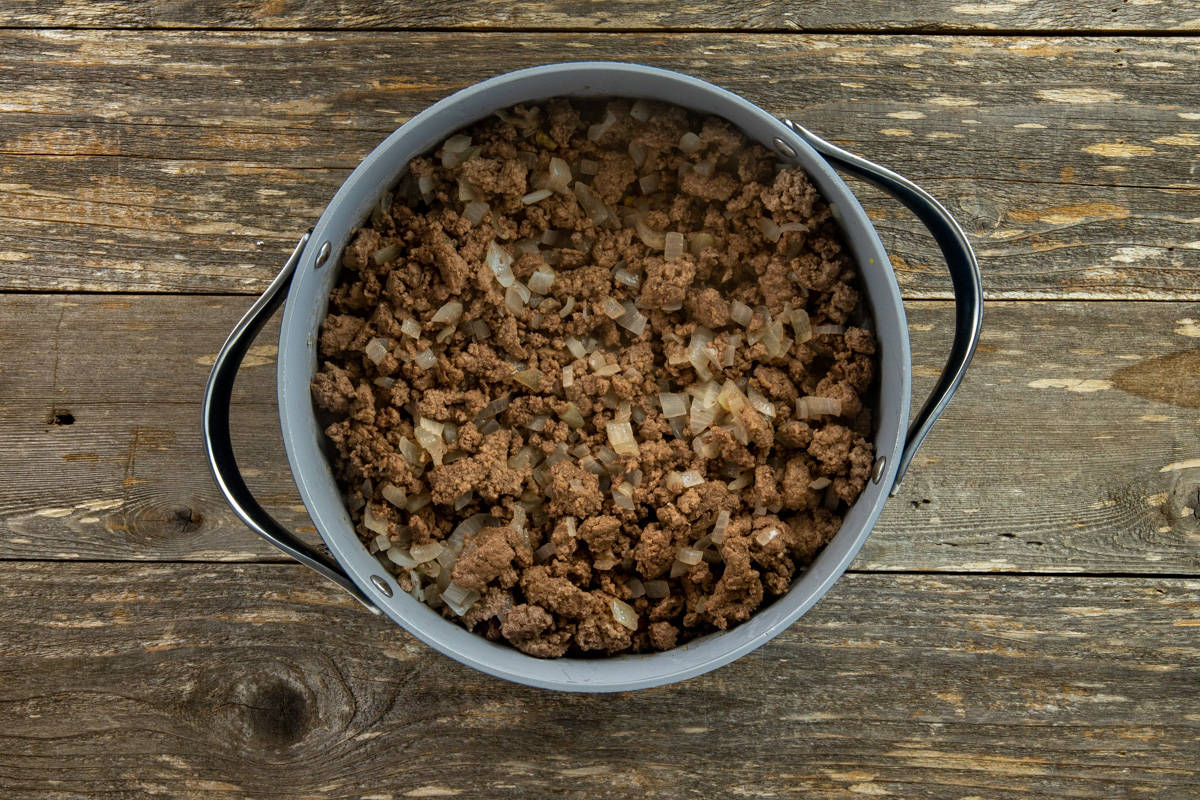 Ground beef and chopped onions cooked in a skillet.