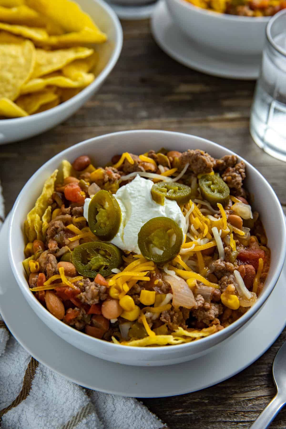 Taco soup in white bowl garnished with corn chips, sour cream, and jalapeno slices.