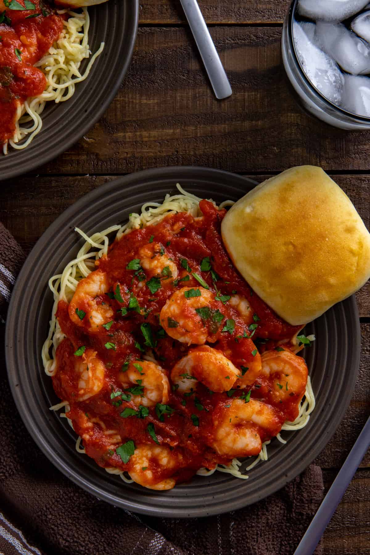 Shrimp spaghetti on a brown plate with a dinner roll on the side.