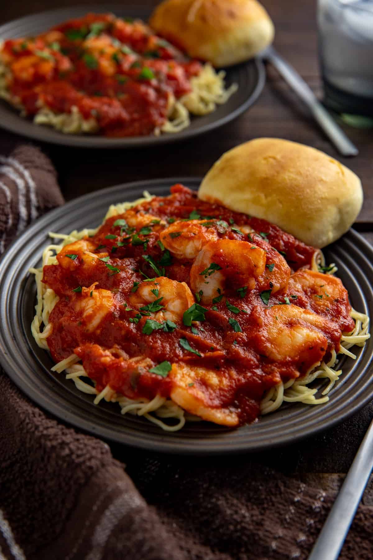 Shrimp spaghetti on a brown plate with a dinner roll on the side.