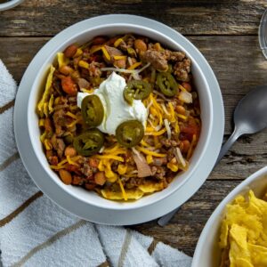 Taco soup in white bowl garnished with corn chips, sour cream, and jalapeno slices.