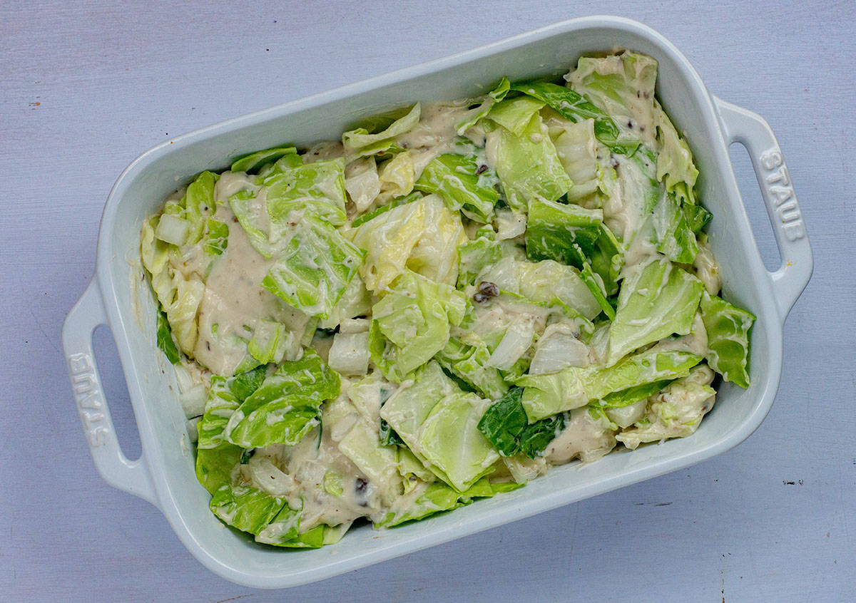 Chopped cabbage and onions with creamy soup mixture in white rectangular casserole dish.
