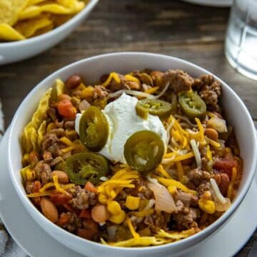 Taco soup in white bowl garnished with corn chips, sour cream, and jalapeno slices.