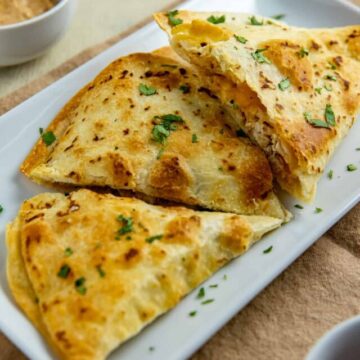 Three quesadillas on white rectangular plate garnished with parsley flakes.