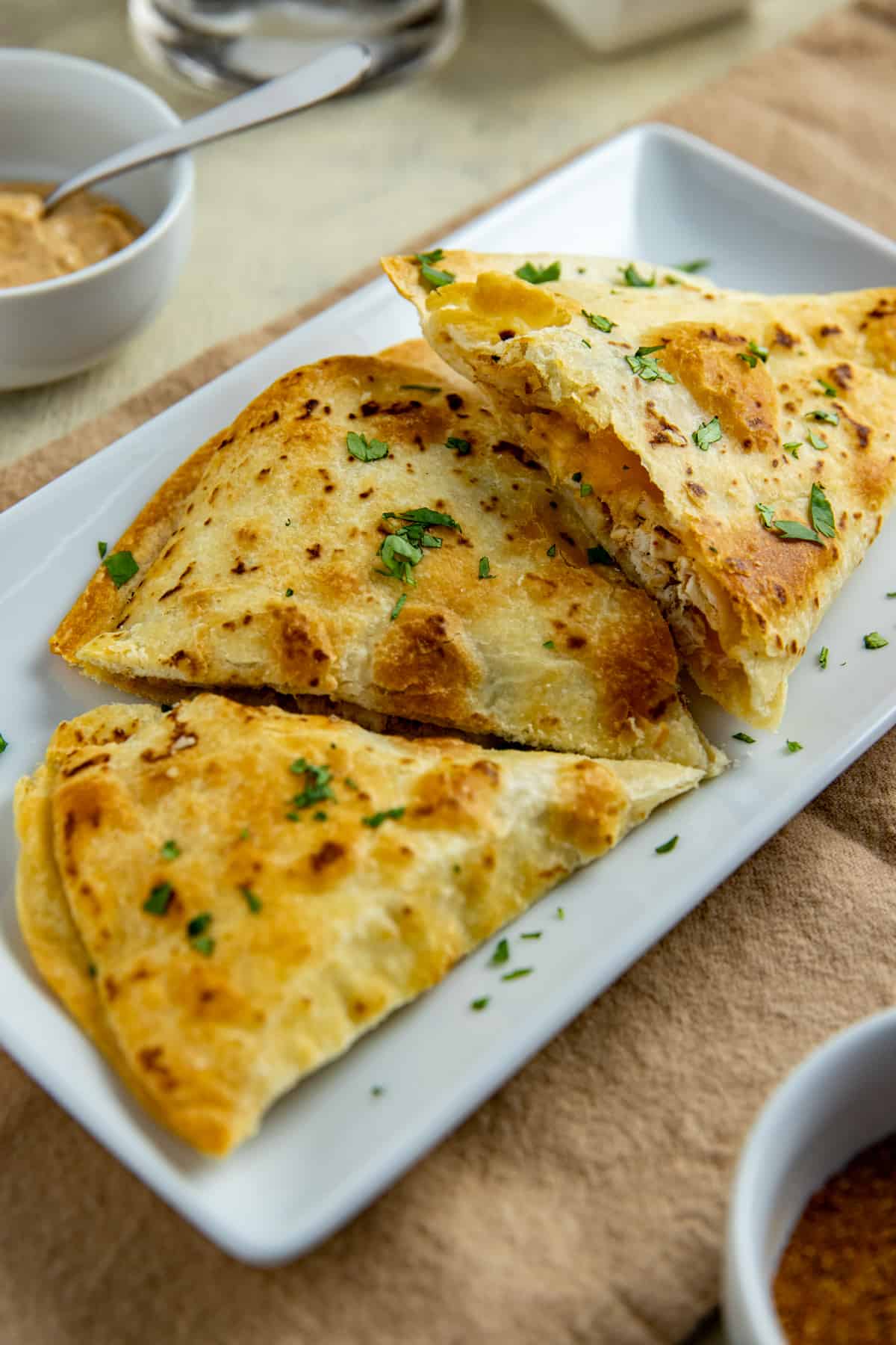 Three quesadillas on white rectangular plate garnished with parsley flakes.