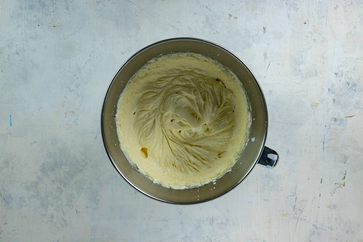Butter, sugar, eggs, and vanilla extract blended in a stainless steel mixing bowl.