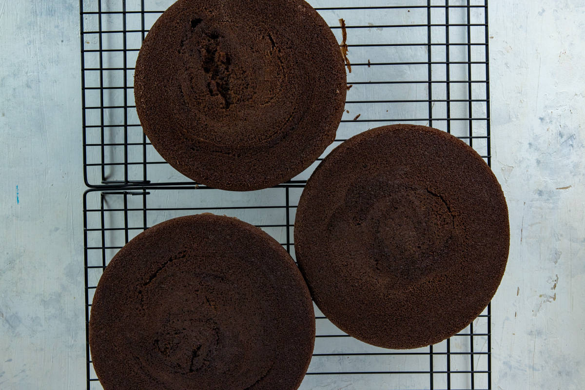 Three baked cake layers cooling on a cooling rack.