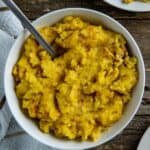 Cooked corn casserole in white bowl with spoon inserted into the casserole.