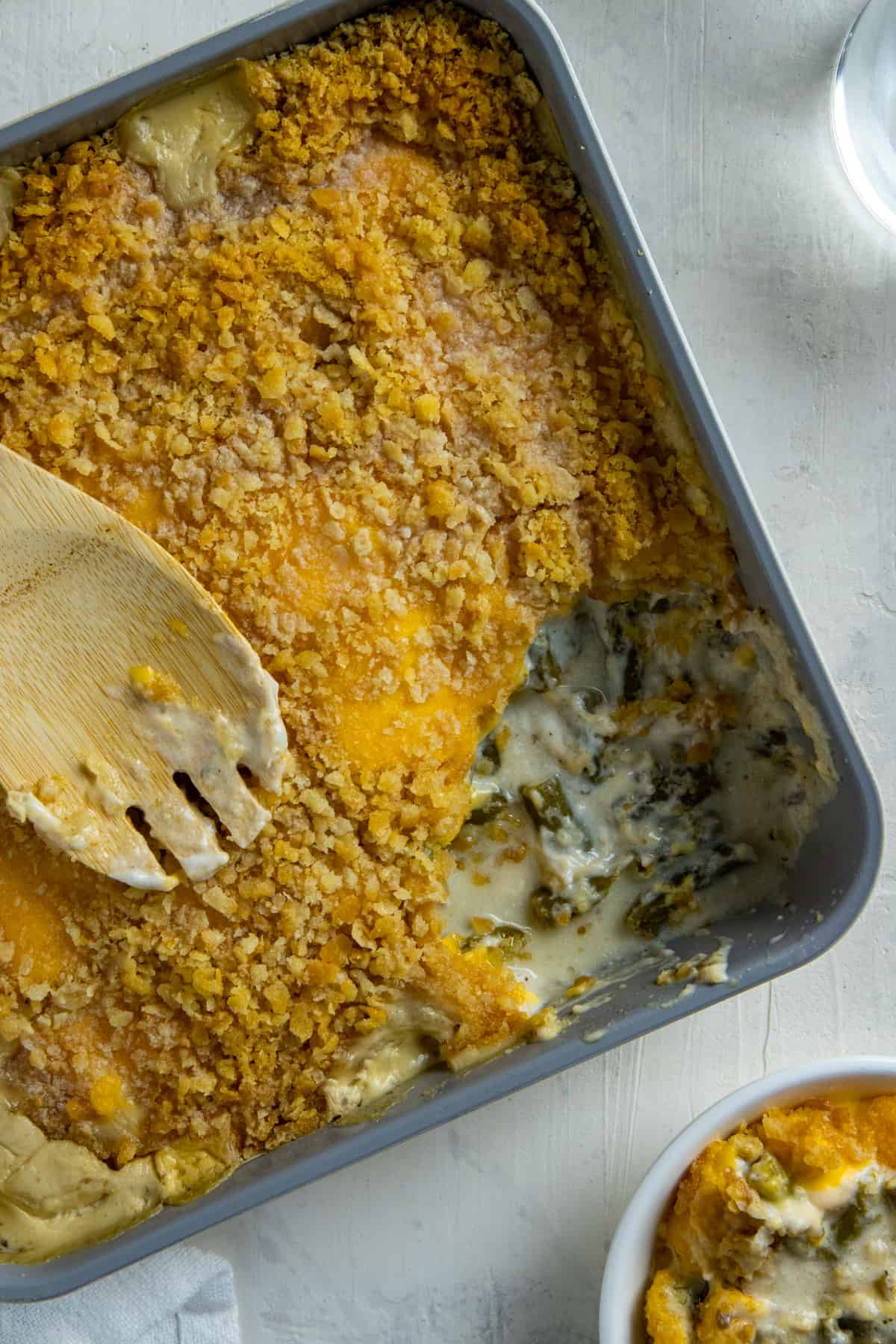 Cooked green bean casserole in square casserole dish with one serving removed. A wooden serving spoon is resting on top of the casserole.