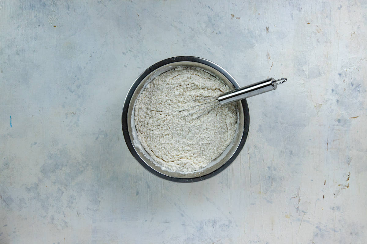 Flour, baking soda, baking powder, and salt blended in a stainless steel mixing bowl.