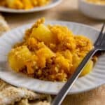 A serving of pineapple cheese casserole on round white plate with fork.