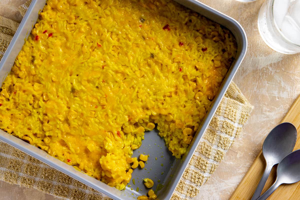 Baked corn and rice casserole in square casserole dish with a serving in the corner that's been scooped out.