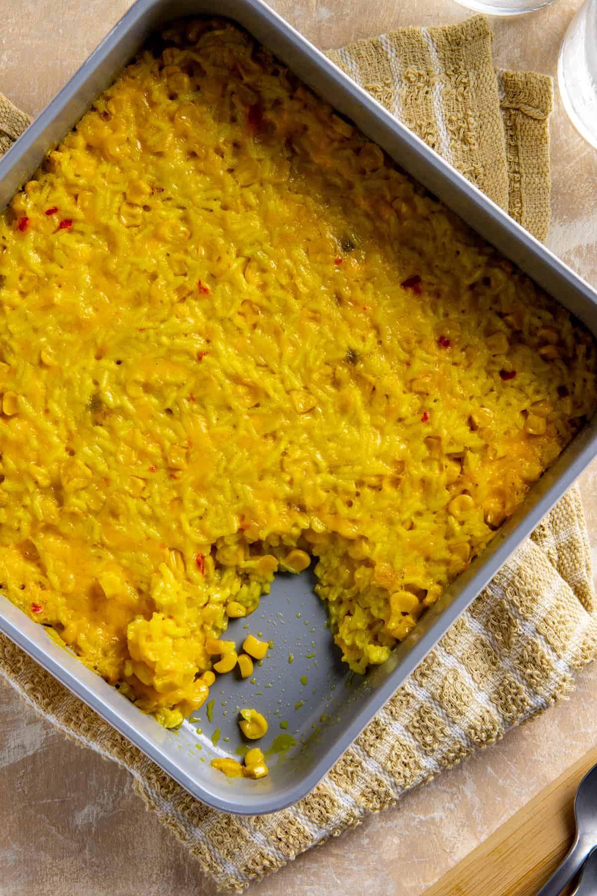 Baked corn and rice casserole in square casserole dish with a serving in the corner that's been scooped out.