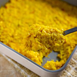 Square pan with cooked corn and rice casserole. Spoon scooping out a serving.