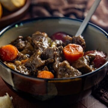 Cooked beef stew in a brown bowl with a spoon in the bowl.