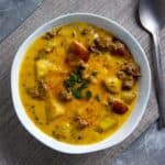 Cooked cheeseburger soup in white bowl with spoon in the background.