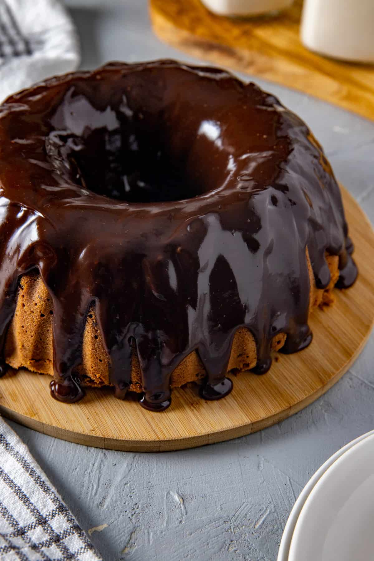 Whole baked cake with ganache glaze all over.  Cake on a round wooden cake platter.
