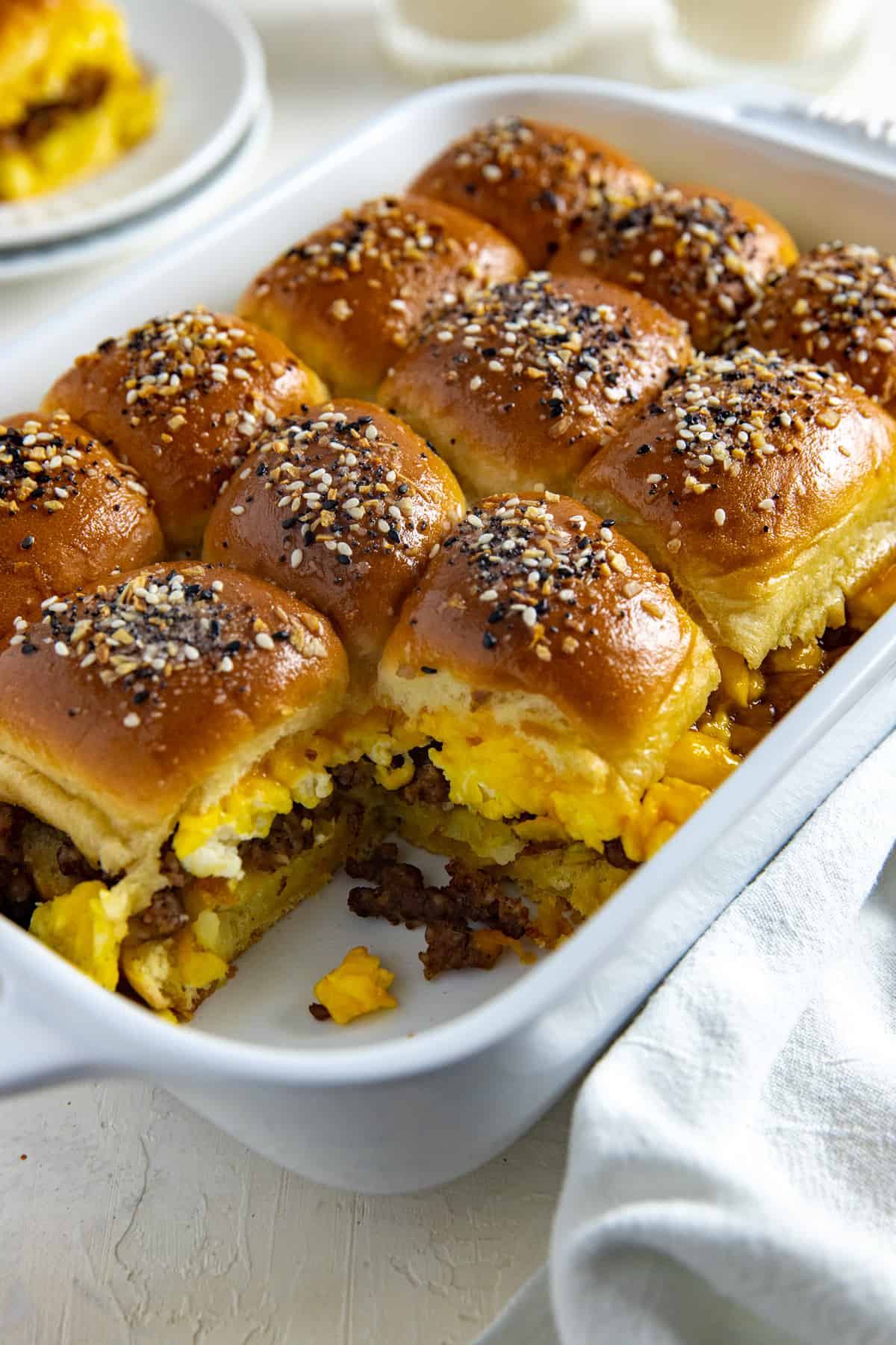 Twelve baked sliders in a casserole dish with one removed.
