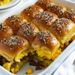 Twelve baked sliders in a casserole dish with one removed.