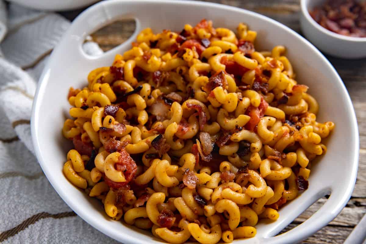 Macaroni and tomatoes topped with crumbled bacon in serving dish.