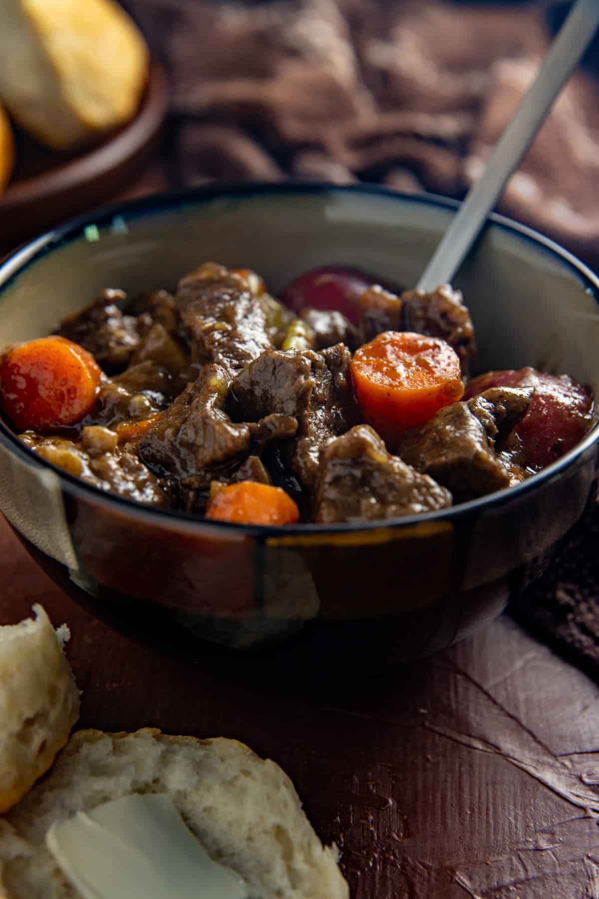 Cooked beef stew in brown bowl with biscuits on the side.