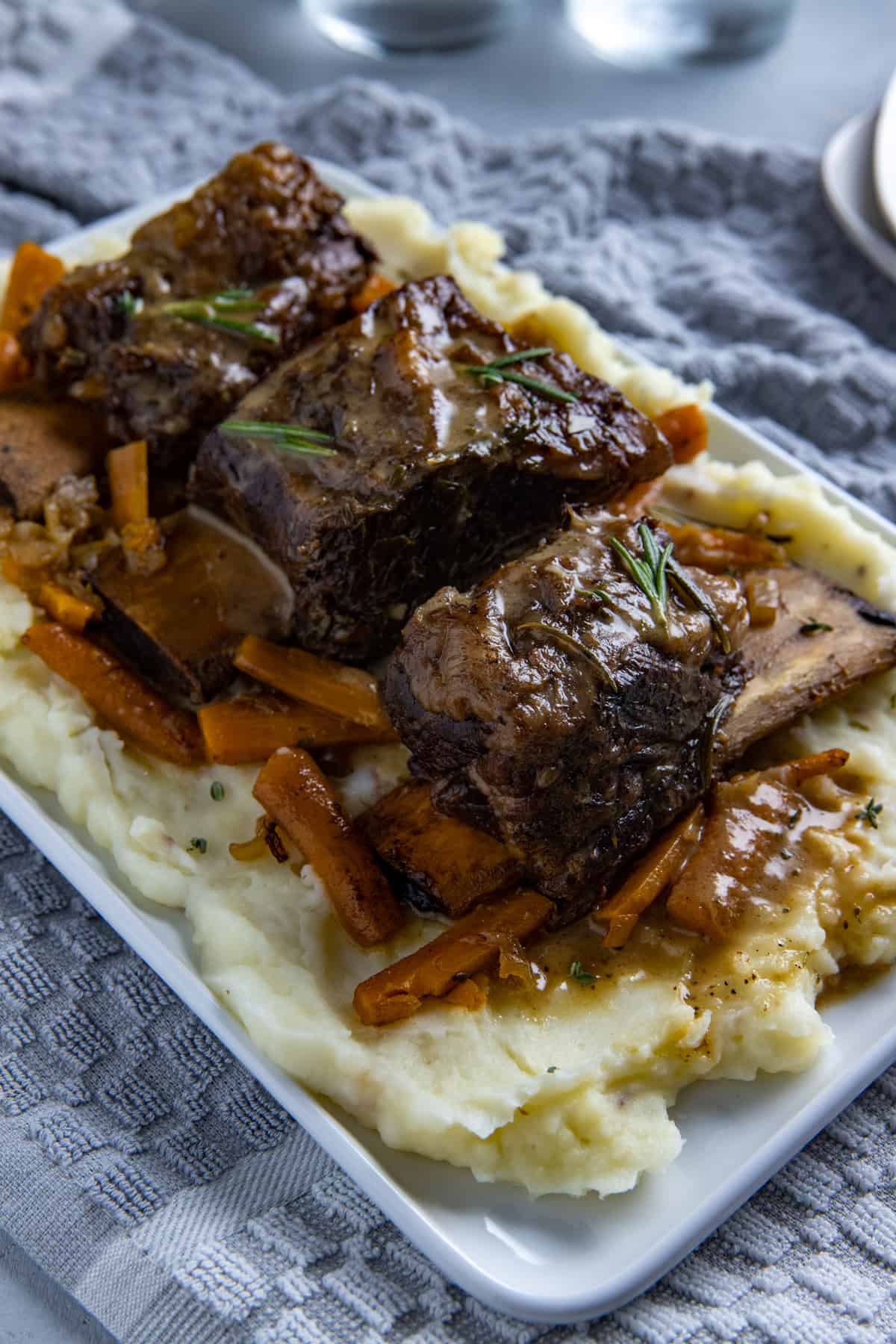 Cooked beef ribs on a bed of mashed potatoes with onions and carrots scattered around.