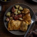 Two baked chicken thighs on a brown plate with roasted potatoes on the side.