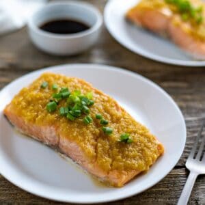 One salmon fillet on a white plate topped with miso ginger apple topping.