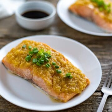 One salmon fillet on a white plate topped with miso ginger apple topping.
