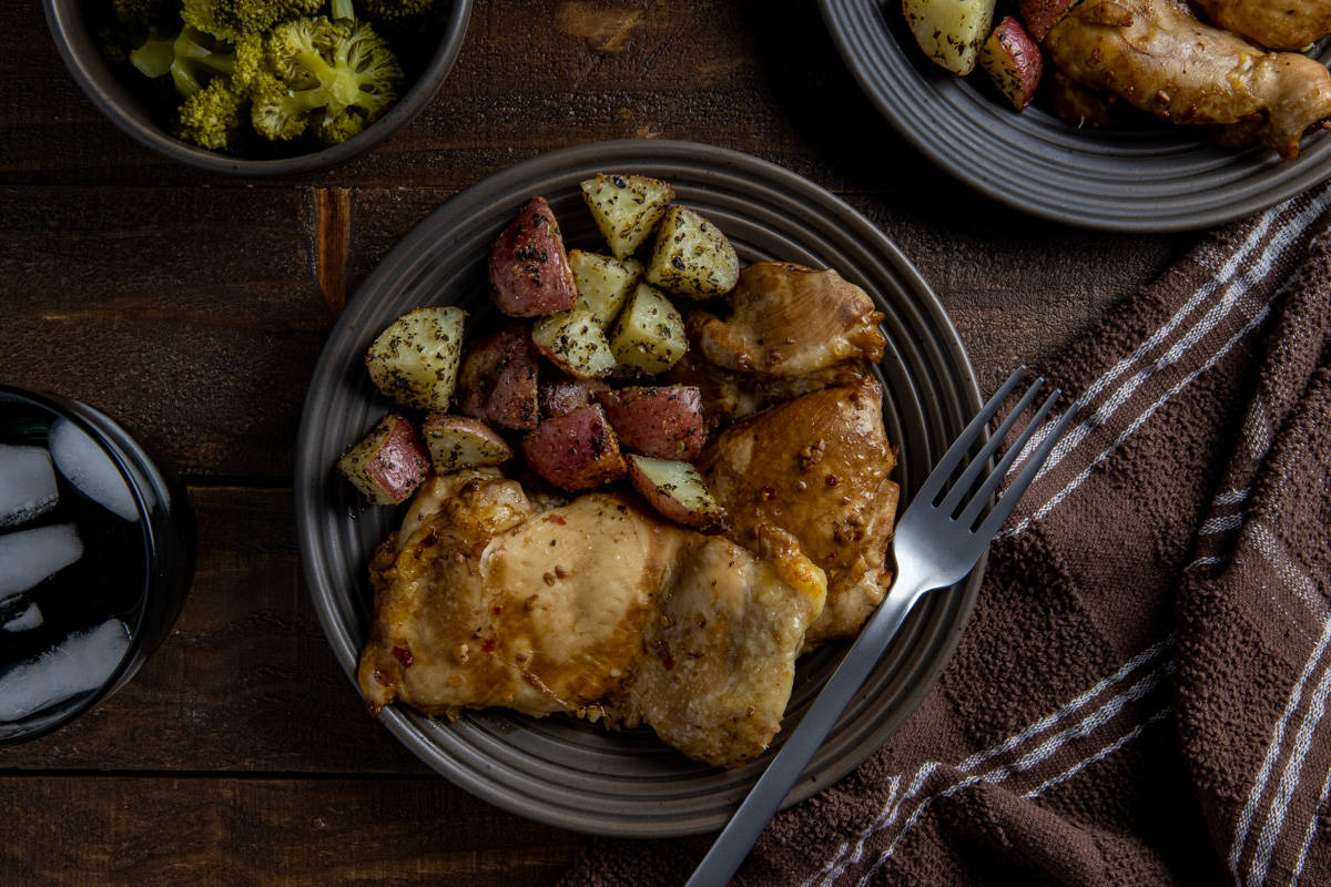 Two baked chicken thighs on a brown plate with roasted potatoes on the side.