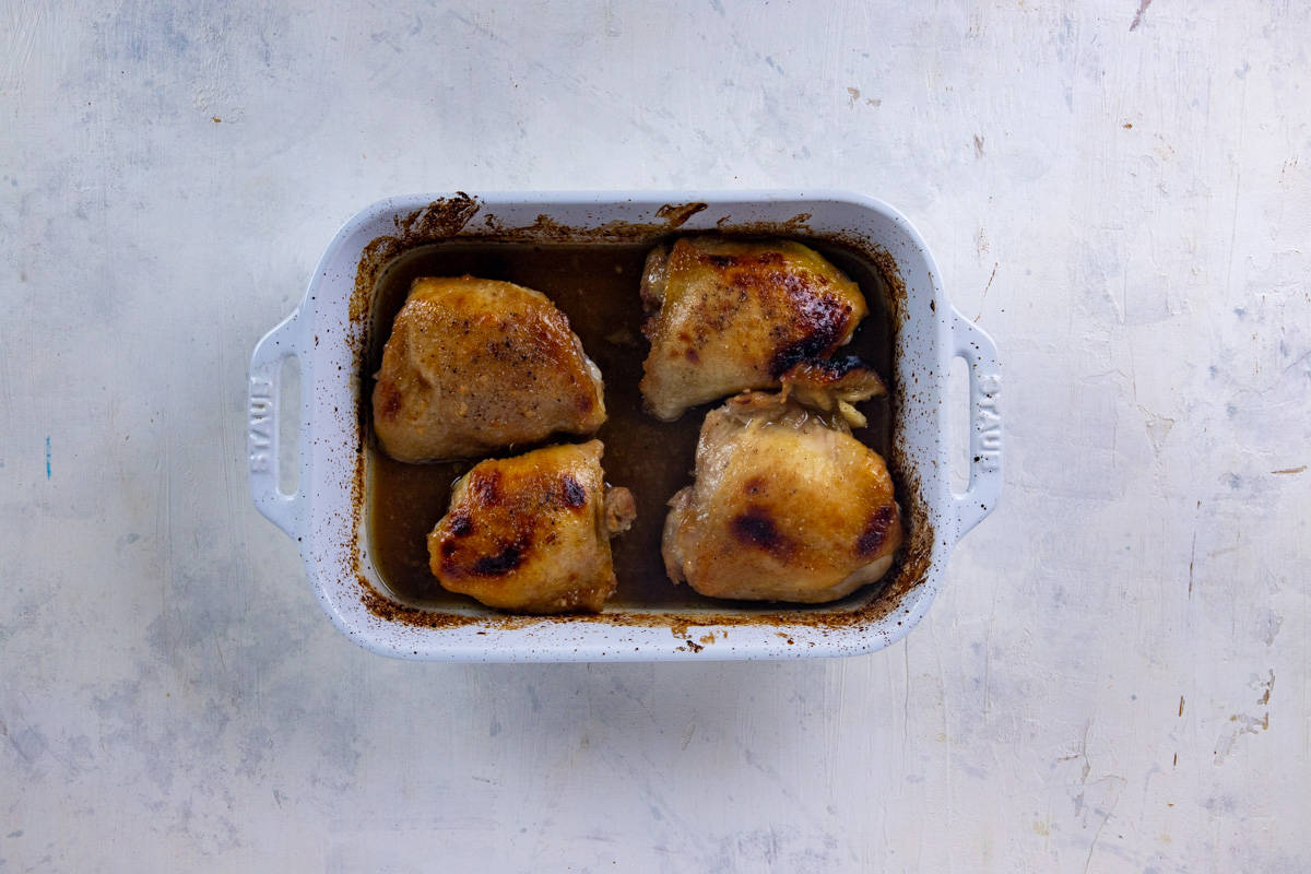 Four baked chicken thighs in white casserole dish.
