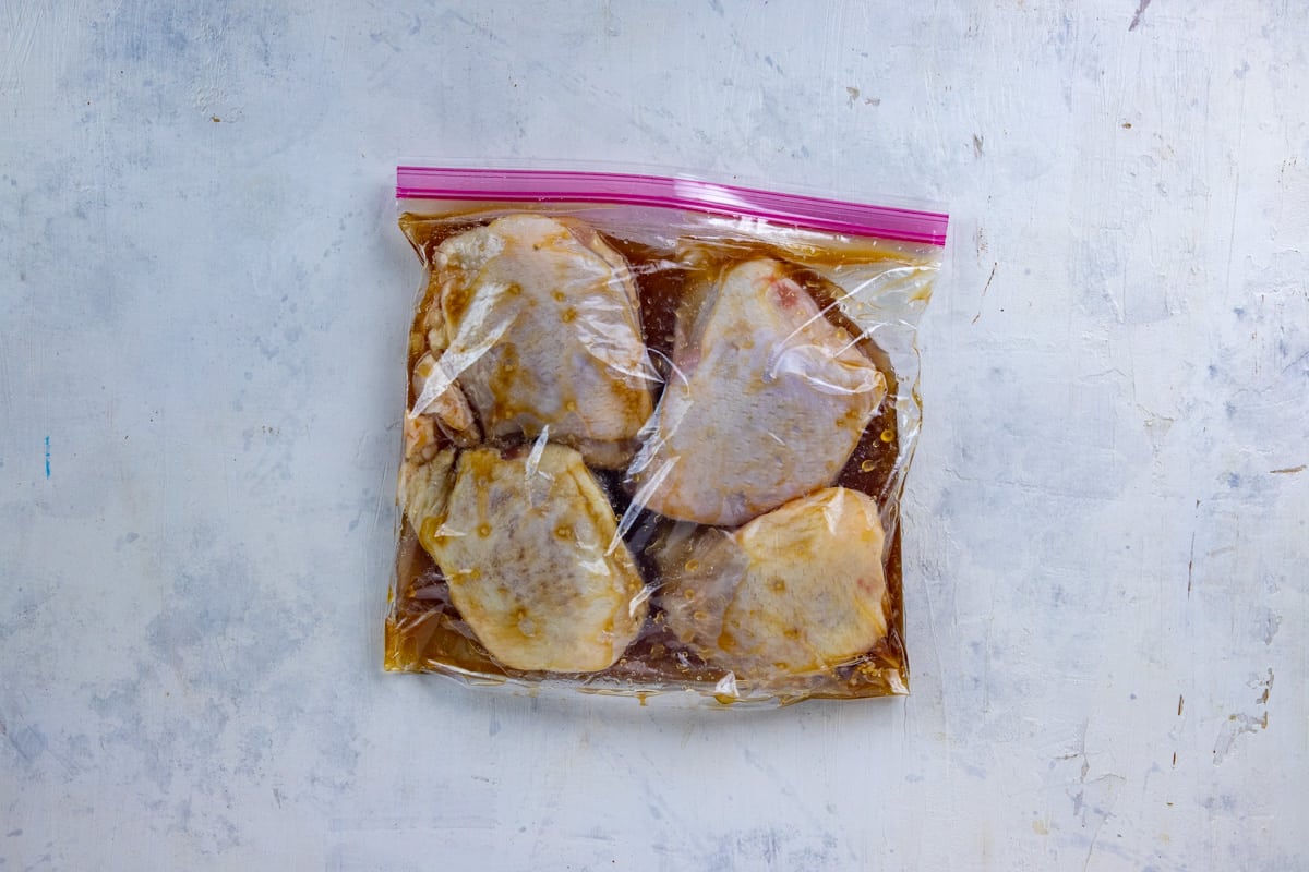 Four raw chicken thighs in marinade in a gallon ziplock bag.