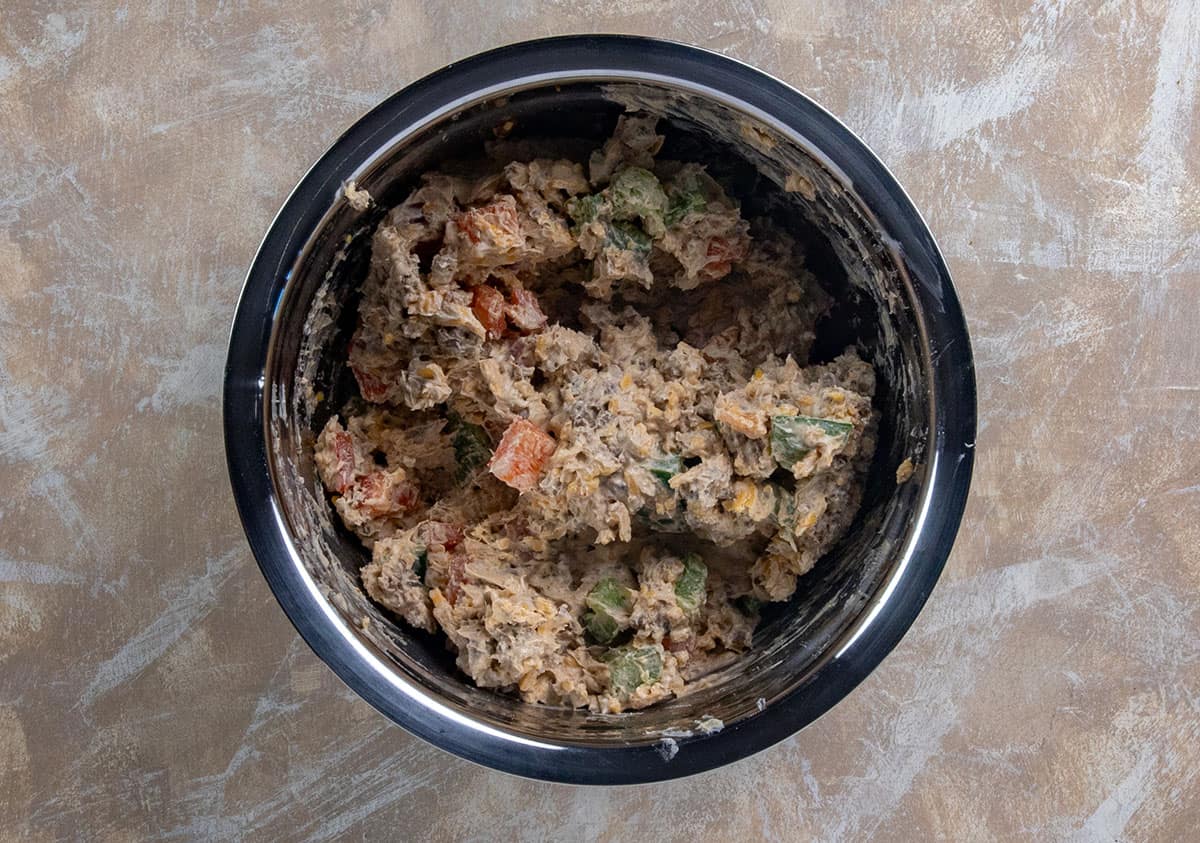 Taco meat, cream cheese, shredded cheese, red and green bell peppers mixed up in a stainless steel bowl.