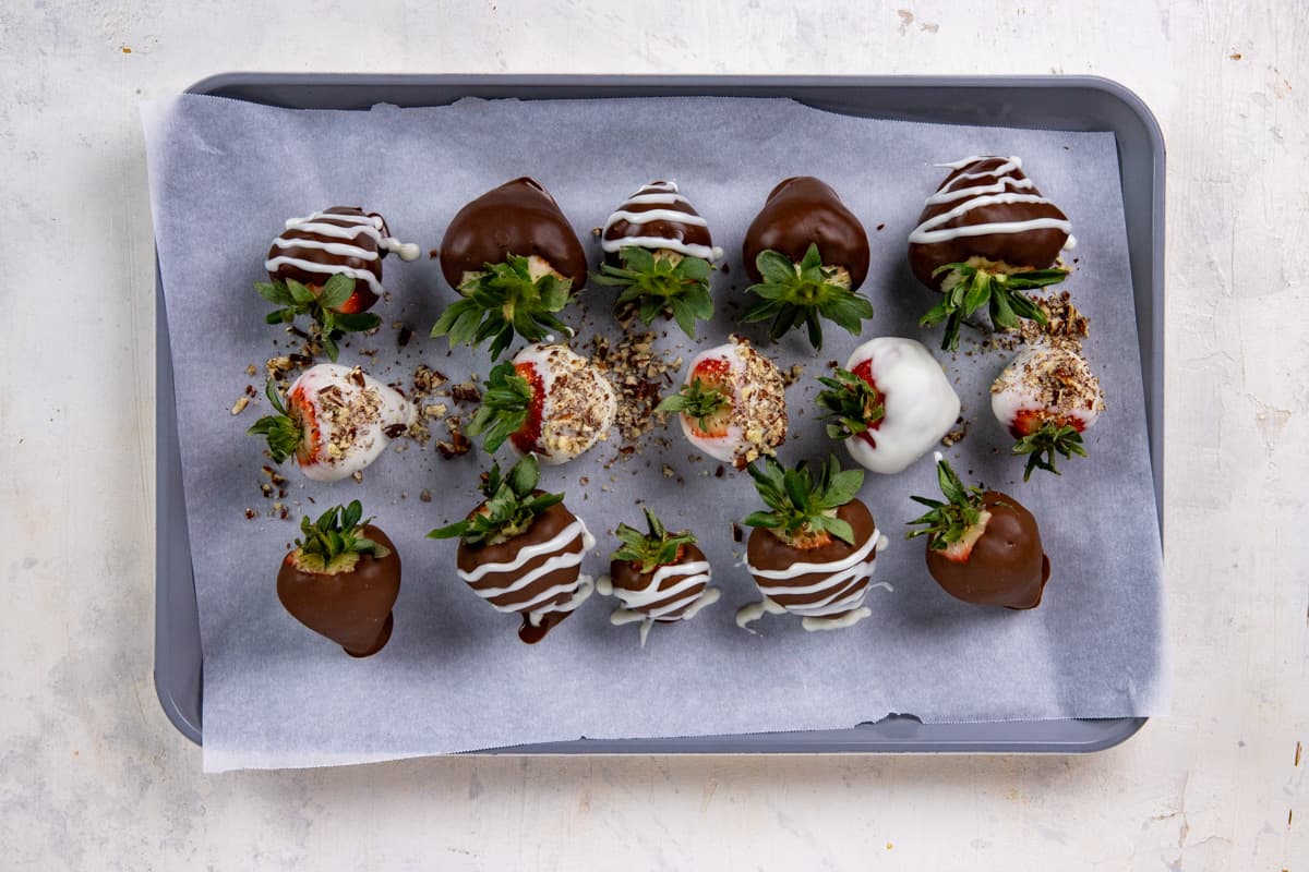 Ten chocolate dipped and decorated strawberries on parchment lined cookie sheet.