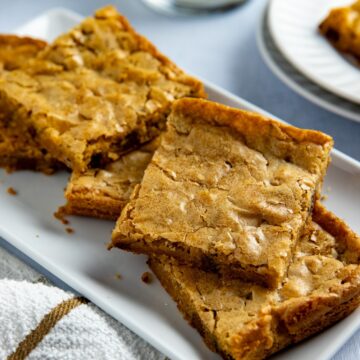 Several baked and sliced blondies stacked on a white rectangular platter.