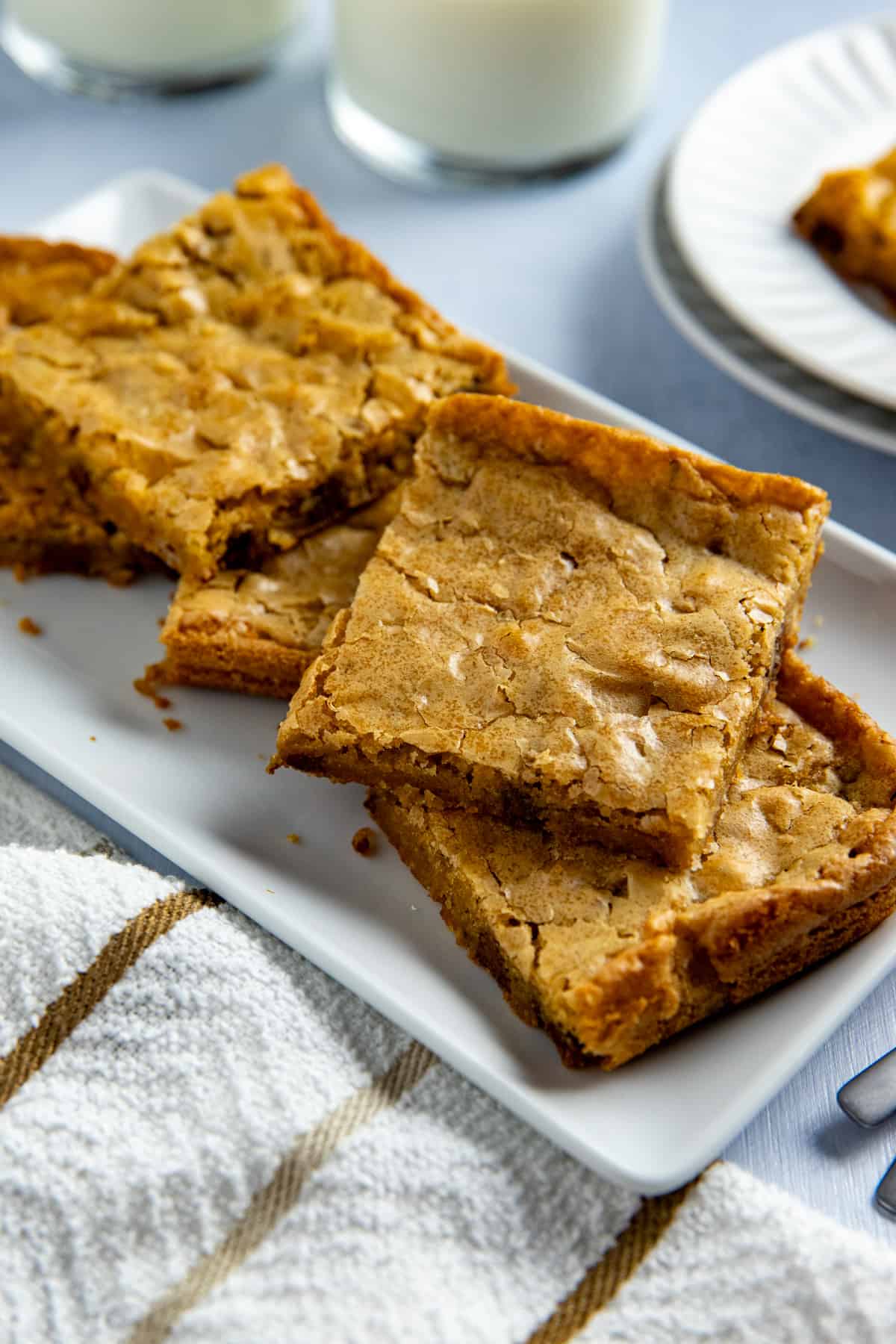 Several baked and sliced blondies stacked on a white rectangular platter.