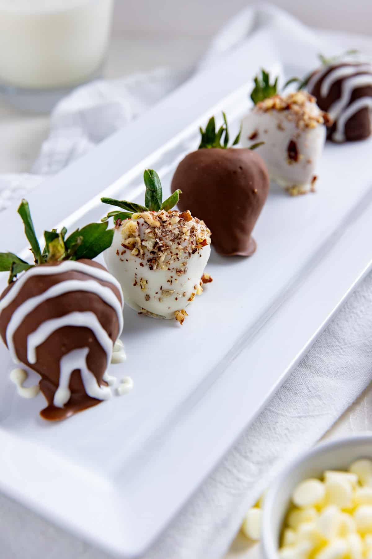 Chocolate covered strawberries with white chocolate drizzle and chopped pecans on a rectangular white serving platter.