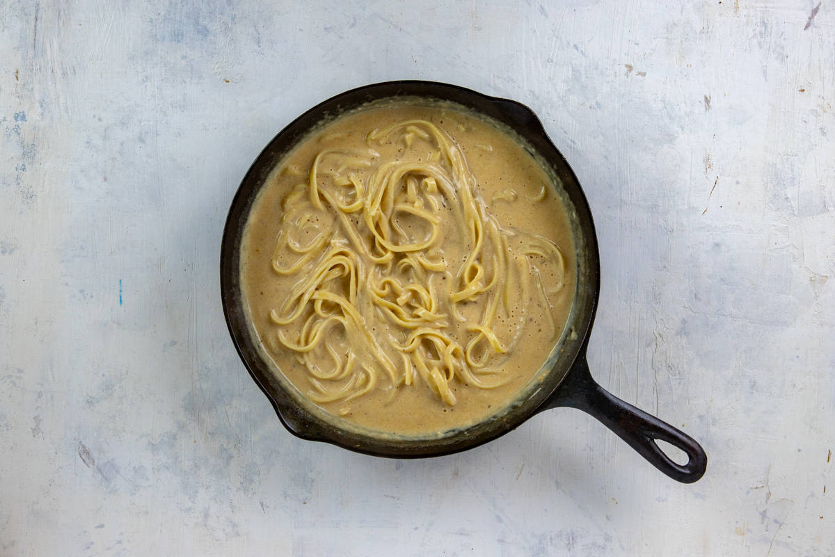 Cooked pasta mixed in with the alfredo sauce in a cast iron skillet.