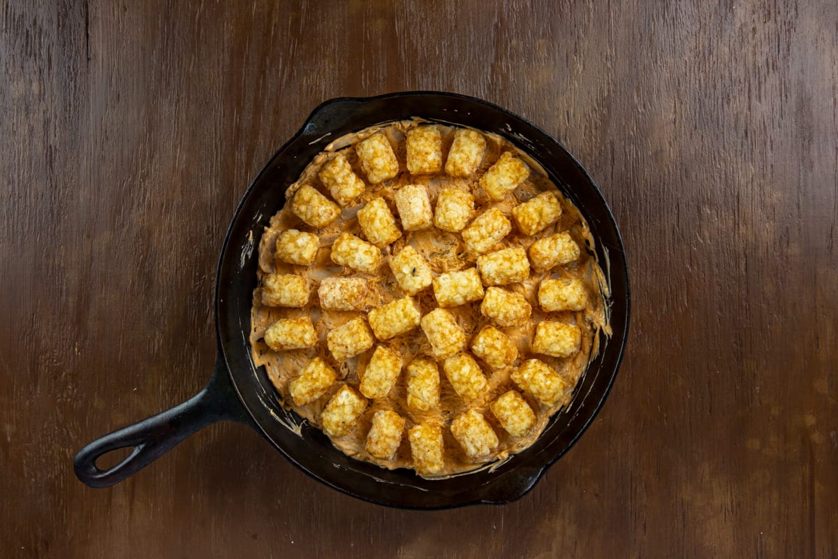 Frozen tater tots on top of the chicken mixture in a skillet.