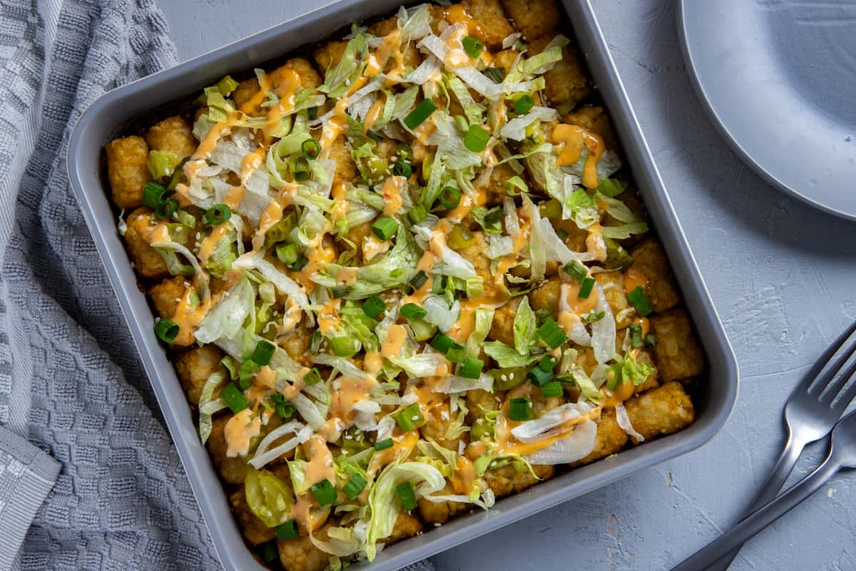 Baked tater tot casserole with shredded lettuce and Thousand Island dressing on top.
