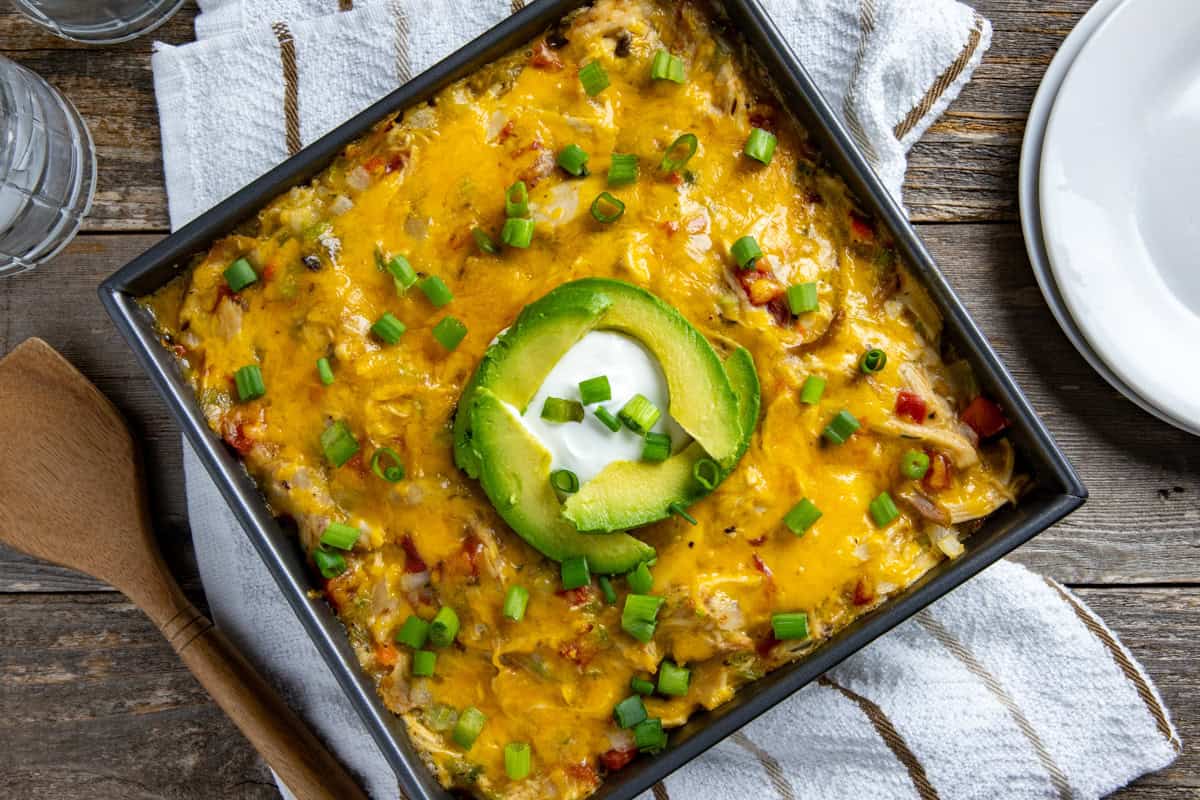 Baked King Ranch Chicken Casserole in square metal baking dish garnished with sliced avocado and dollop of sour cream.