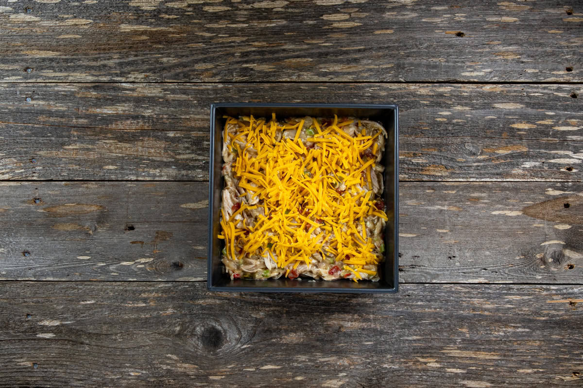 Layers of corn tortillas, cheese, and chicken mixture in square baking dish.
