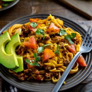 Mexican Spaghetti on brown plate with sliced avocado on the side.