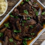 Cooked sliced roast topped with mushrooms and sliced portobella mushrooms on a white serving platter.