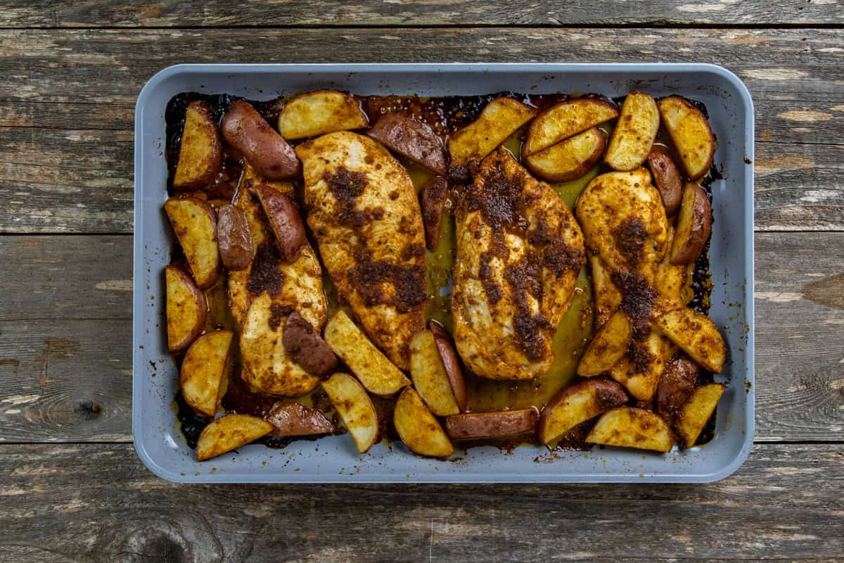 Cooked seasoned chicken and potato wedges on a sheet pan.