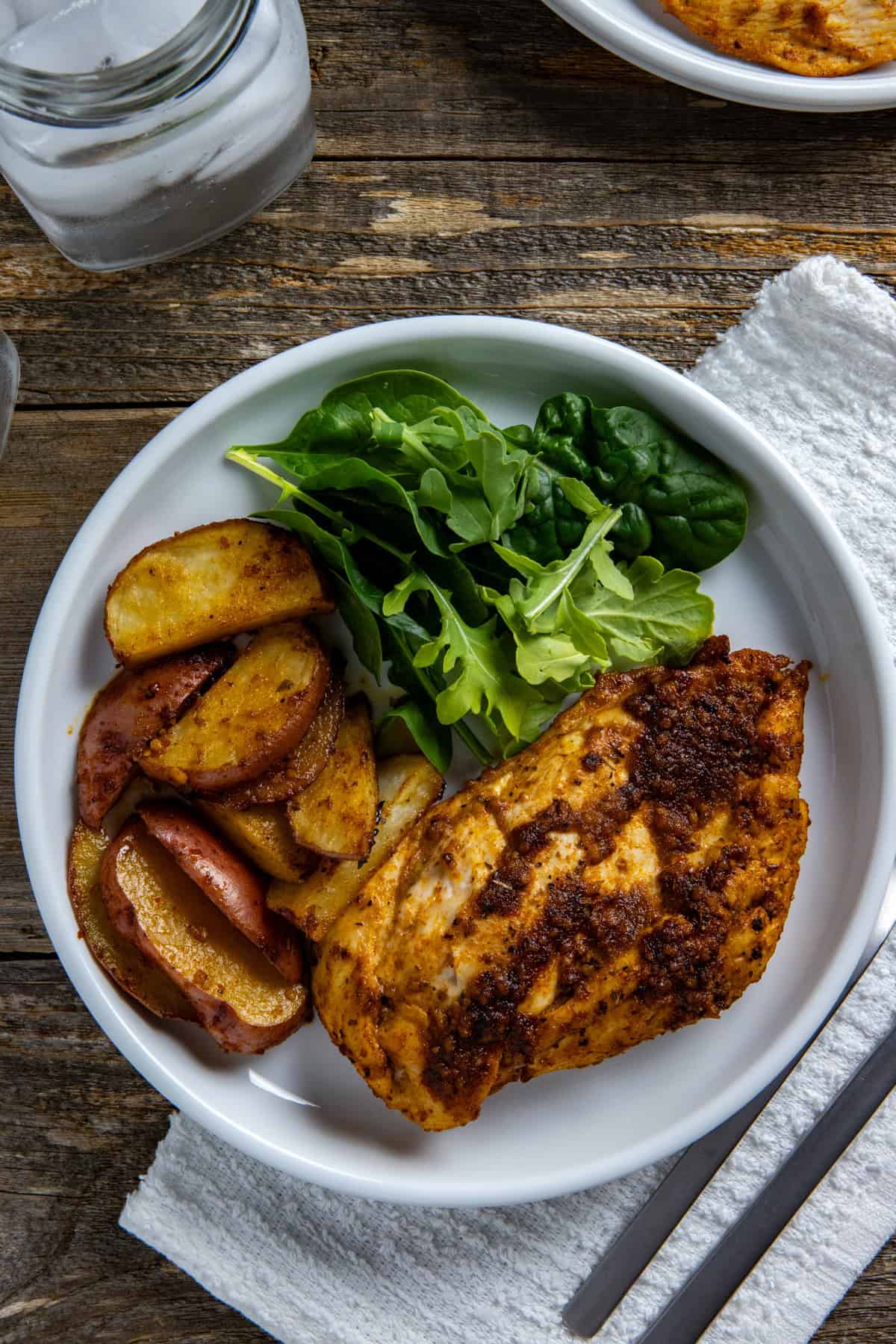 Baked chicken, potatoes, and a green salad on a white plate.