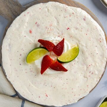 Whole pie topped with strawberry and lime wedges on a round wooden board.