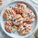 Baked and frosted cookies with sprinkles on a white plate.