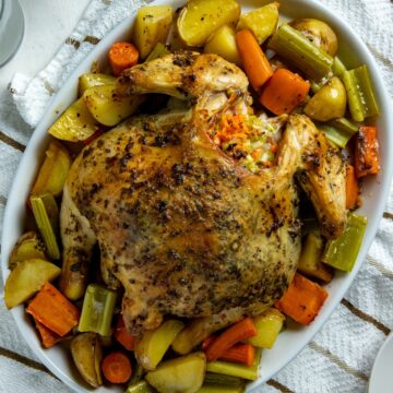 Baked whole chicken on top of chopped carrots, potatoes, and onions in a sheet pan.